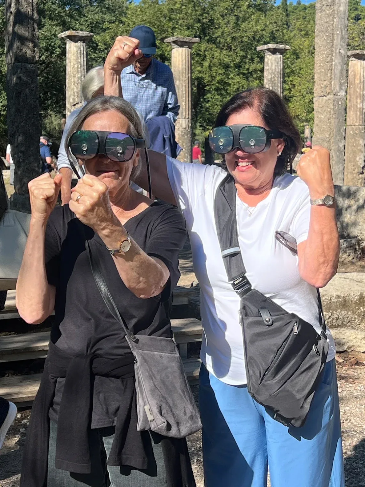 Two smiling grandmothers wearing VR glasses among the columns of Ancient Olympia